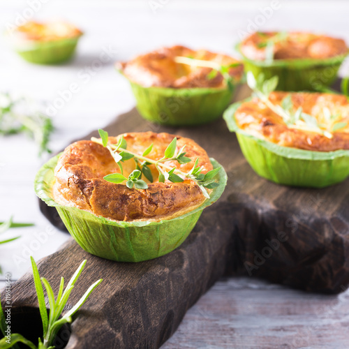 Savory cheddar cheese and leek mini quiches with thyme on dark wooden cutting board