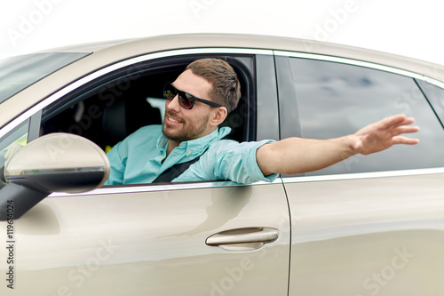 happy man in shades driving car and waving hand