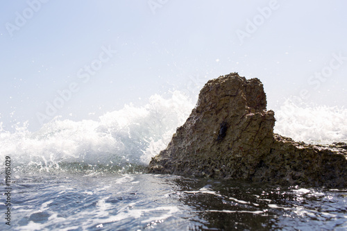 Sea wave splashing over the shore rocks with a high sea spray