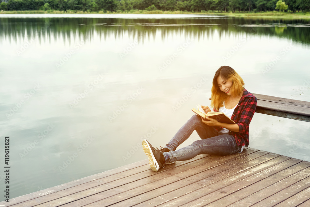 Young girl reading book and sitting on wood balcony by river