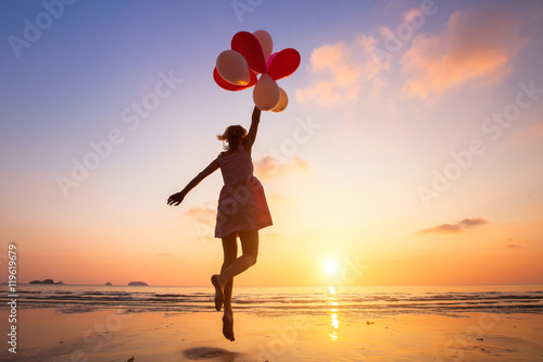imagination, happy girl jumping with multicolored balloons at sunset on the beach, fly, follow your dream photo