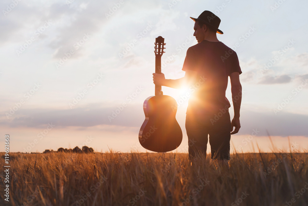 Fototapeta premium silhouette of musician with guitar at sunset field