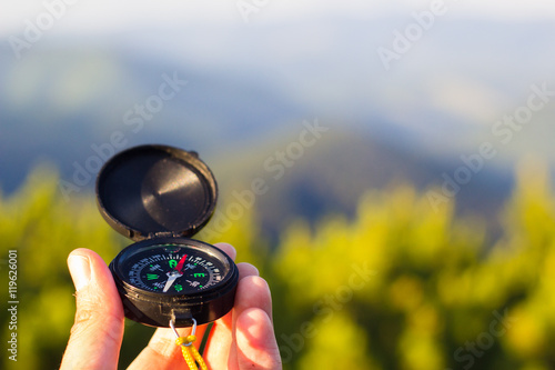 Hand holding compass on summer mountains background