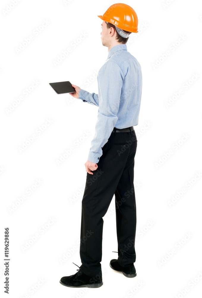 Backview of business man in construction helmet stands and enjoys tablet or using a mobile phone. Curly businessman in a light jacket and a helmet reads works with the tablet on the site. Backview of business man in construction helmet stands and enjoys tablet or using a mobile phone. Curly businessman in a light jacket and a helmet reads works with the tablet on the site.