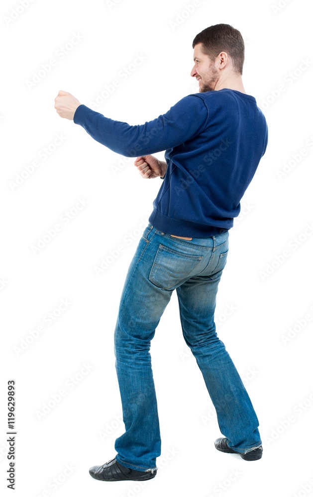 back view of standing man pulling a rope from the top or cling to something.  bearded man in blue pullover pulls the rope side. Stock Photo
