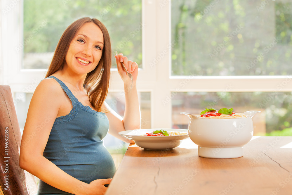 Pregnant woman is eating huge portion of pasta with tomato sauce