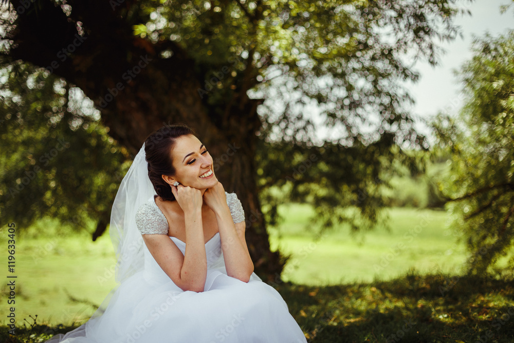 Thoughtful smiling bride holds her head while sitting on the law Thoughtful smiling bride holds her head while sitting on the law
