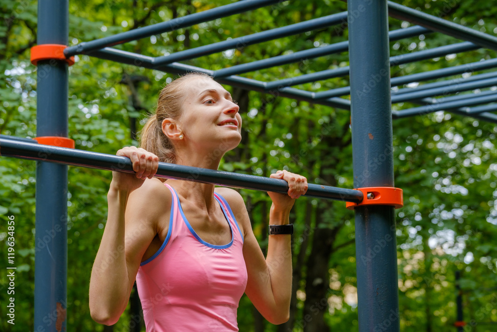 Young slim woman pulls on horizontal bar in a park