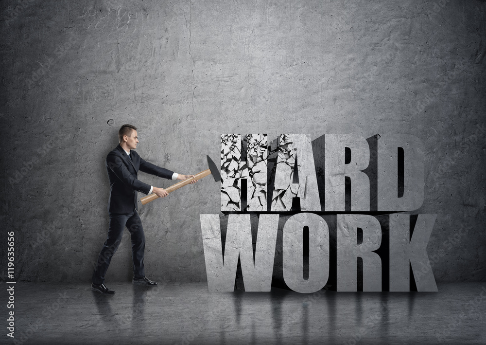 Side view of young businessman crashing 3D concrete 'hard work' words with a hammer Side view of young businessman crashing 3D concrete 'hard work' words with a hammer