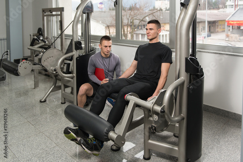 Personal Trainer Takes Notes While Man Exercising Legs