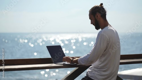 young businessman using his laptop on the waterfront on sea background