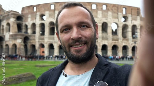 Happy man taking selfie photo and recording video near Colosseum, slow motion 
