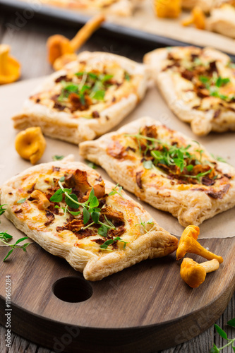 Homemade tarts of puff pastry with seasonal chanterelle mushrooms, cheese, thyme and onion on rustic wooden table, selective focus