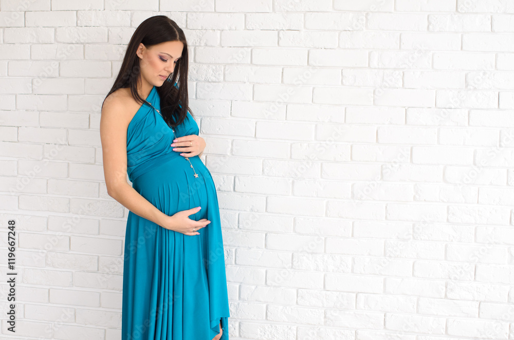 pregnant woman in turquoise dress on white brick wall background pregnant woman in turquoise dress on white brick wall background
