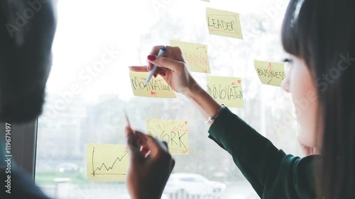 Three business people having a meeting in office. They are standing in front of glass wall with post it notes, pointing and discussing - business, teamwork, brainstorming concept