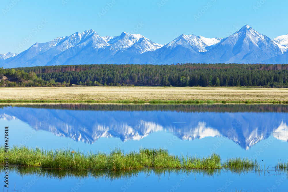 Spring landscape with the reflection of the snow-capped Eastern Sayan Mountains in the river