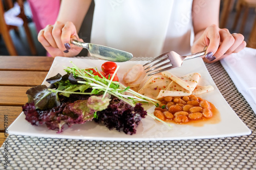 Woman having healthy breakfast, green salad with grilled chicken breast, chili bologna and baked beans