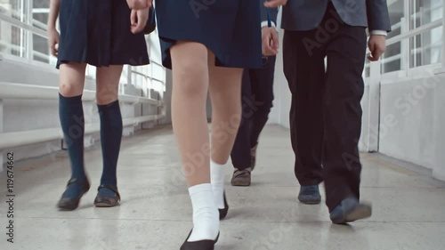Low section of legs of little schoolgirls wearing uniform skirts with knee-high socks walking along hallway with schoolboys in twill pants heading to lessons photo