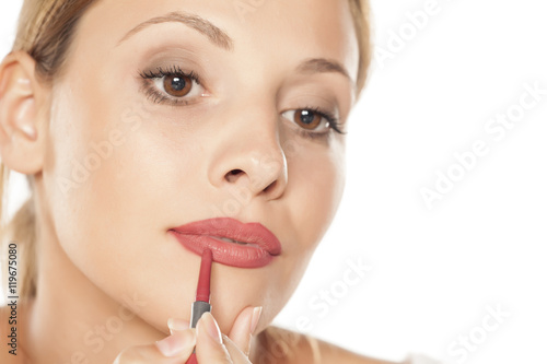 young beautiful woman outlining her lips with a pencil