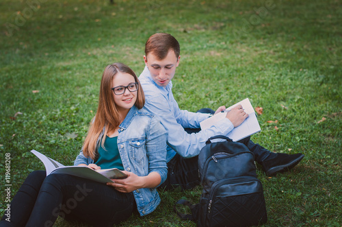 students guy and the girl in the park sitting on the grass and reading a book. Education concept