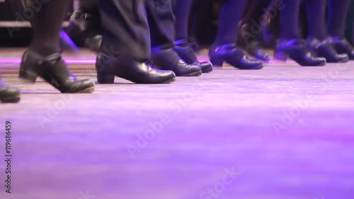One row of people doing Irish dance with traditional step shoes. Close up single line of dancing feet on stage. Music, tradition and culture of Ireland. Celtic show on wooden floor