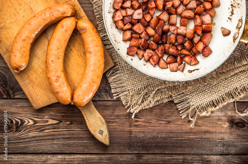 Foto Fried sausages sliced in a cube on a frying pan on a wooden background