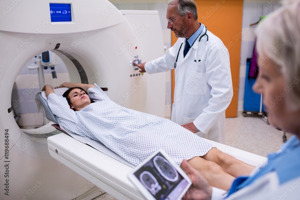 Doctor looking at brain MRI scan of a patient lying on bed in hospital Doctor looking at brain MRI scan of a patient lying on bed in hospital