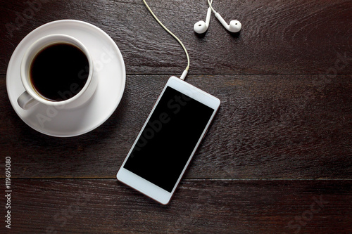 Top view white smartphone,black coffee,earphones on wood table.