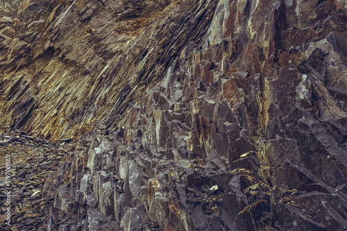 Arid strata volcanic rock cliff and stone debris in an old abandoned basalt quarry near the Racos extinct volcano in Brasov county, Romania.