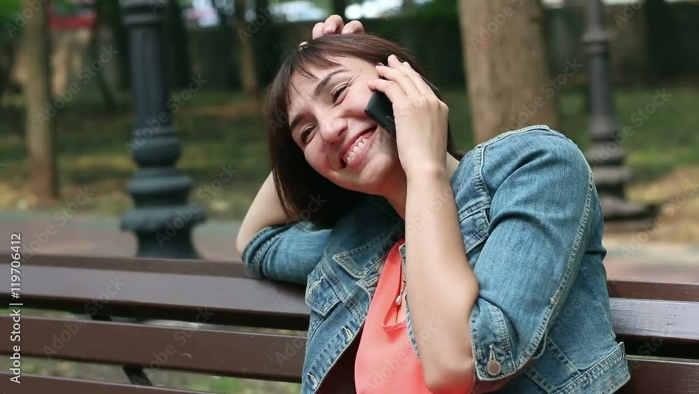 The girl speaks on a mobile while sitting on a bench The girl speaks on a mobile while sitting on a bench