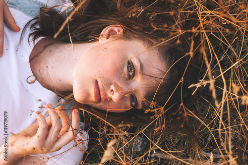 Beauty Young Woman with Brown Hair in Golden Field at Sunset.