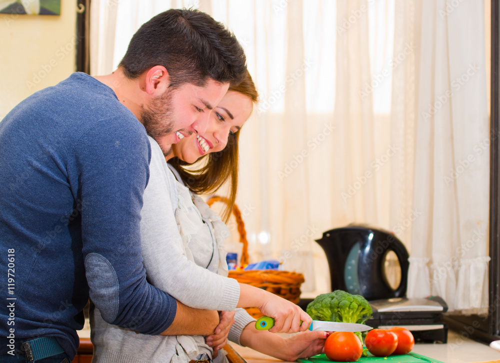Attractive young couple embracing happily while chopping vegetables together, cooking with love concept Attractive young couple embracing happily while chopping vegetables together, cooking with love concept