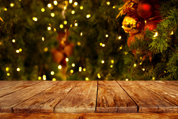 Christmas and New year background with empty dark wooden deck table over christmas tree and blurred light bokeh. Empty display for product montage. Rustic vintage Xmas background.