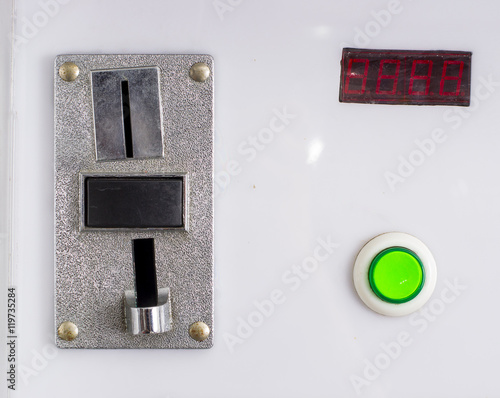 A closeup of a metal coin slot panel from a coin operated machine with entry and exit slots and button on an isolated background
