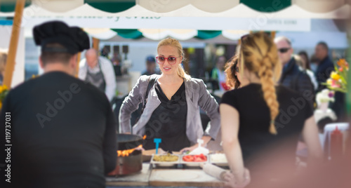 Beautiful blonde caucasian lady buying freshly prepared meal at a local street food festival. Urban international kitchen event in Ljubljana, Slovenia, in summertime. photo