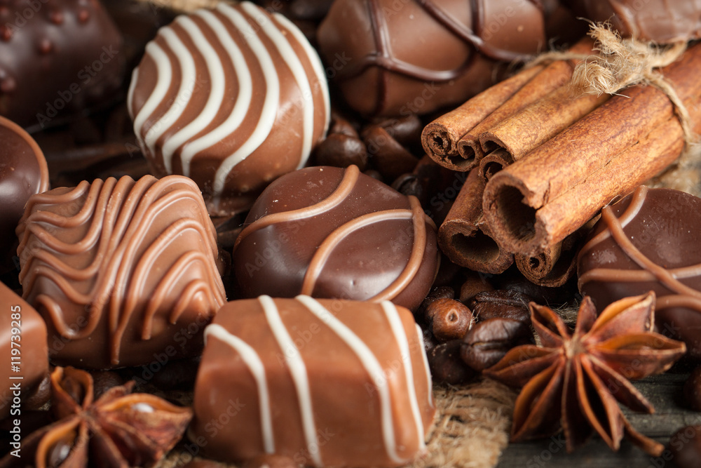 Assortment of dark, white and milk chocolate stack, chips. Chocolate and coffee beans on rustic wooden sacking background. Spices, cinnamon. Selective macro focus. Chocolates background. Sweets