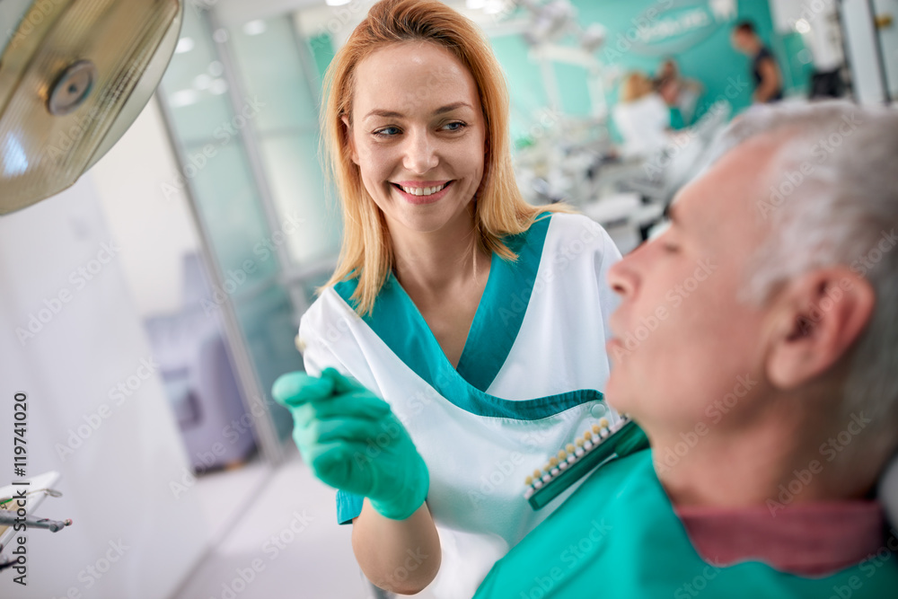 Fototapeta premium Female dentist shows to patient closest color of teeth for dentu