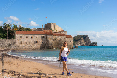 A Beautiful young girl is walking on the beach over the old town