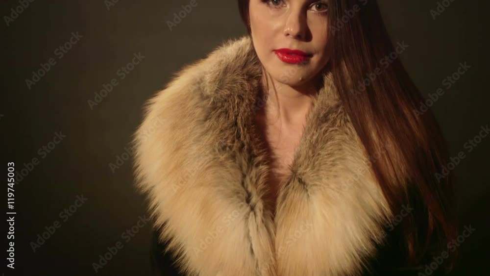 Pretty brunette woman in jacket with fur collar posing on dark background tilt up Pretty brunette woman in jacket with fur collar posing on dark background tilt up