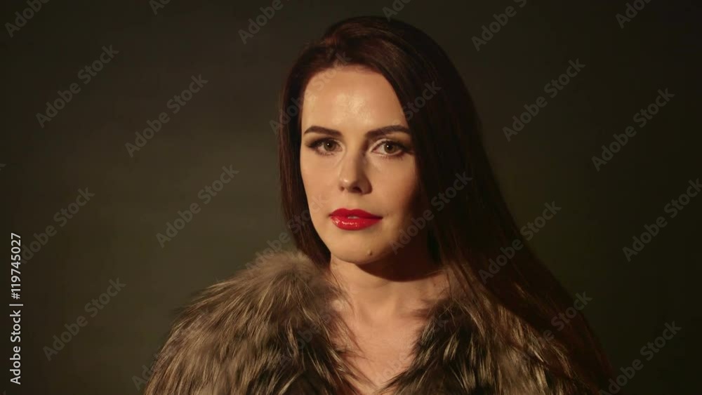 Beautiful woman in lingerie and fur jacket posing on dark background tilt down from woman's face to body Beautiful woman in lingerie and fur jacket posing on dark background tilt down from woman's face to body