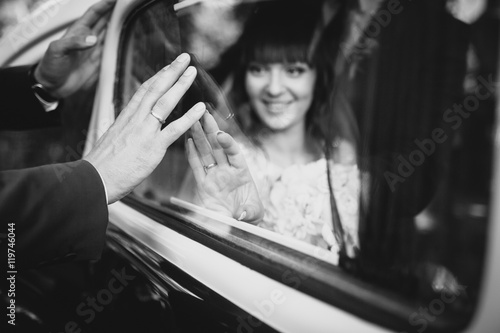 Beautiful happy young bride and groom kissing in retro auto. Embracing near old limousine. Brown color car.