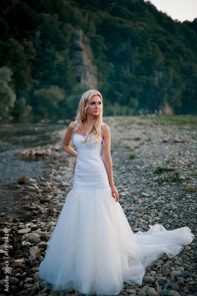 Pretty bride in amazing white dress on mountain river's coast