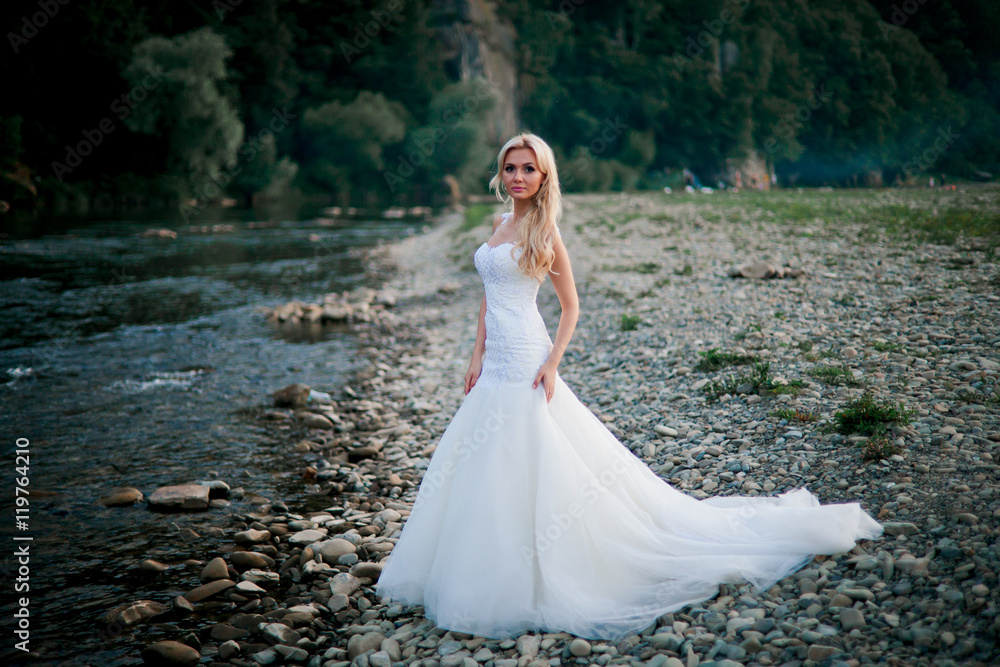 Lovely bride in amazing white dress on mountain river's coast