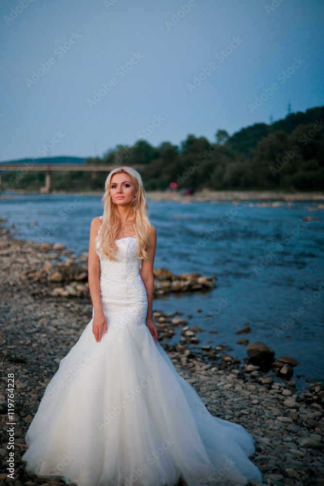 Charming bride in amazing white dress on mountain river's coast