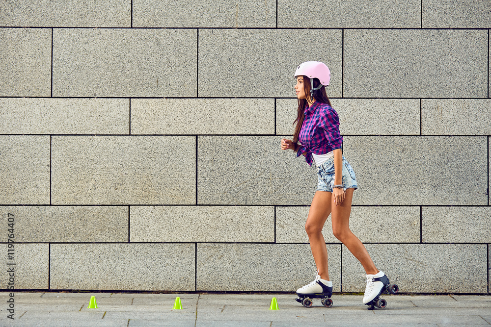 Beautiful young woman on roller skates and a pink helmet. Stylish girl in hipster retro roller skates skating in extreme urban park. Beautiful young woman on roller skates and a pink helmet. Stylish girl in hipster retro roller skates skating in extreme urban park.