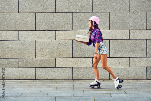 Fototapeta Naklejka Na Ścianę i Meble -  Fast delivery of sportive girl on roller skates. Young woman on roller skates with box or pizza in hands.