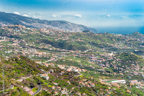 Aerial view down valley in Portuguese Madeira Island in Atlantic Ocean. High angle view down hillside into green valley with houses and roads in Madeira Portugal, image for travel business concept