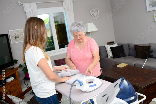 cheerful young girl ironing and helping with household chores an elderly woman at home