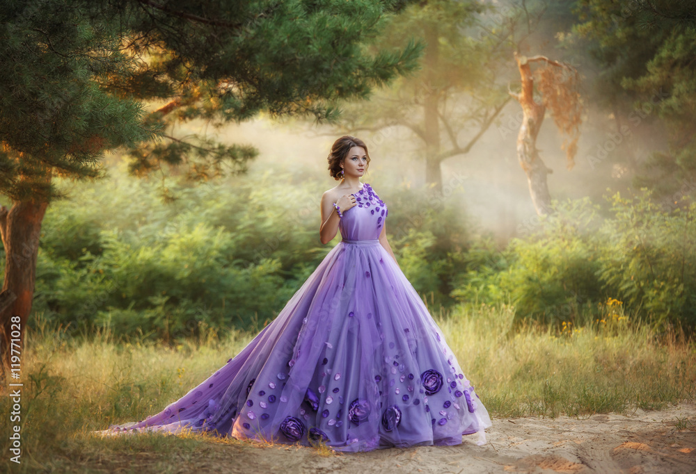 Fototapeta premium Beautiful, young, brunette in a luxurious, purple, long dress. Fairy Photo. Creative toning. Queen walking in the fairy forest.
