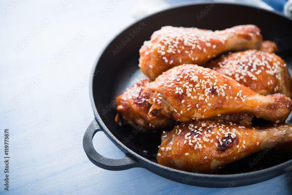 Baked spicy chicken legs with sesame in cast iron frying pan on blue wooden background close up. Baked spicy chicken legs with sesame in cast iron frying pan on blue wooden background close up.